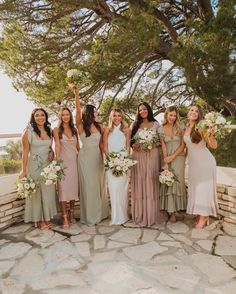 a group of women standing next to each other in front of a stone wall holding bouquets