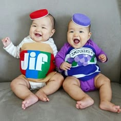 two babies sitting next to each other on a couch wearing matching outfits and smiling at the camera