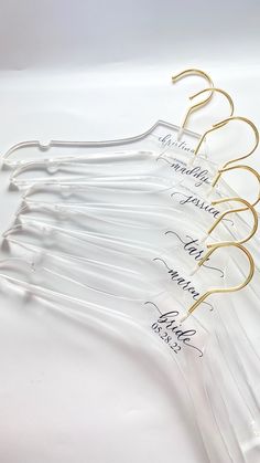 five clear glass hangers with gold colored handles and writing on the sides, all lined up in a row