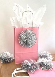 a pink shopping bag with silver pom - poms on it and two white bags