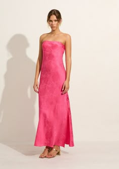 a woman in a pink strapless dress stands against a white wall and poses for the camera