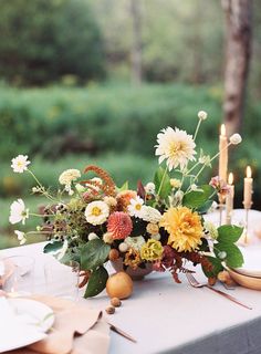 an arrangement of flowers and candles on a table outside in the woods for a wedding reception