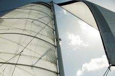 a sailboat with white sails is sailing on the water under a cloudy blue sky