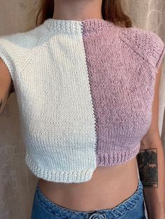 a woman with tattoos standing in front of a wall wearing a pink and white knitted crop top