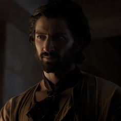 a man with long hair and beard wearing a brown shirt in a dimly lit room