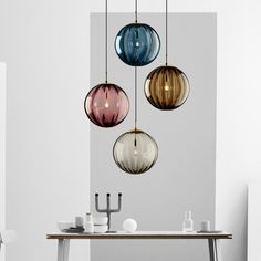 three different colored glass balls hanging from a light fixture over a dining room table and chairs