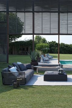 an outdoor living area with couches and tables next to a swimming pool in the background