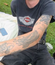 a man with tattoos on his arm sitting in the grass