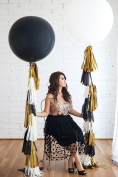 a woman sitting on a chair with balloons in front of her and black and gold tassels around her legs