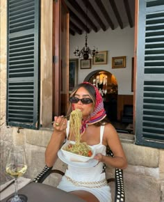 a woman sitting at an outdoor table eating food with a glass of wine in front of her