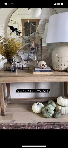 a wooden table topped with white pumpkins under a large lamp and a skull on top