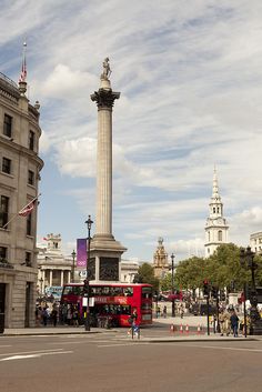 a red double decker bus driving past a tall monument in the middle of a city