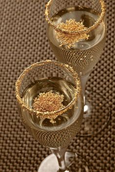 three wine glasses filled with gold flakes on top of a brown cloth covered table