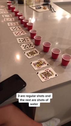 a table topped with red cups filled with playing cards next to a cell phone on top of a counter