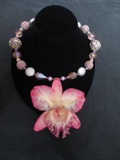 "This is a real cattleya orchid flower that has been preserved in a clear resin. It was originally a clip but I have decided to use it as a pendant for safety. This orchid has shades of salmon pink hues fading into a pale yellow center. The bottom lip is edged in a light berry color. The overall size of the flower measures 4\"x 4\" . I have designed the necklace with pink Swarovski crystals, and different shapes of clay and resin beads that compliment this orchid. There is a silver colored toggle clasp set  with purple crystals. This piece is a real eye catcher. Great piece for a wedding or party." Orchid Jewelry, Clay Beads