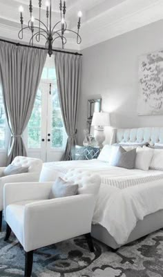 a large white bed sitting under a chandelier in a bedroom next to a window