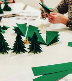 someone cutting out christmas trees with scissors on a table