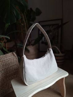 a white handbag sitting on top of a wooden table next to a potted plant