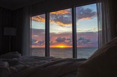 the sun is setting over the ocean from a bed in front of a large window