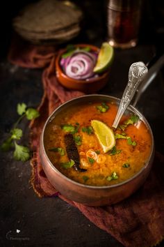 a metal bowl filled with soup and garnished with cilantro, limes, and onions