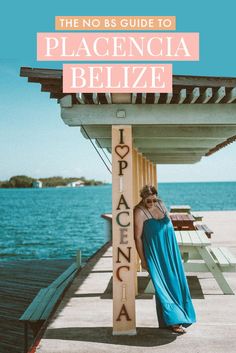 a woman in a blue dress standing next to a sign that reads the no bs guide to placencia belize