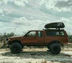 a red truck with a surfboard on the roof parked in front of power lines