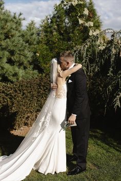 a bride and groom kissing in front of some bushes on their wedding day at the park