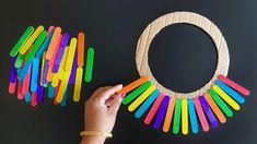 a person holding a wooden circle with colored sticks attached to it, next to a black background