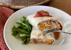 a burrito on a white plate with a fork and some lettuce next to it