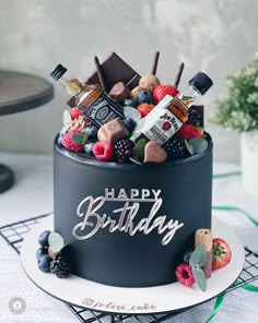 a birthday cake decorated with chocolates, fruit and liquor bottles is on a table