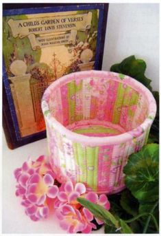 a pink and green basket sitting next to a book