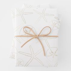 a gift wrapped in white paper with brown ribbon and starfishs on it, tied up