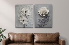 two large white flowers are hanging on the wall next to a brown leather couch in a living room