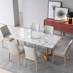 a marble dining table surrounded by white chairs in a room with gray carpet and artwork on the wall