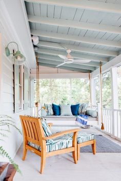 a porch with white furniture and blue pillows on the front porch, including a swing bed