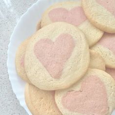 some heart shaped cookies are on a white plate with pink frosting in the middle