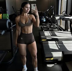 a woman taking a selfie with her cell phone in a gym room while standing next to treadmills