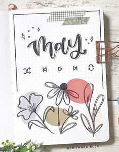 an open notebook with the words may on it and flowers in front of it, next to a plant