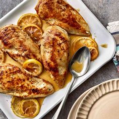 a white plate topped with chicken covered in lemons and sauce next to a fork