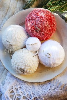 three balls of yarn sitting on top of a plate next to a christmas tree branch