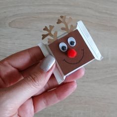 a hand holding up a small brown paper reindeer ornament with red nose and antlers