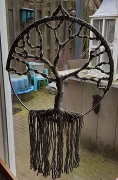 a metal tree with some branches hanging from it's sides, in front of a window