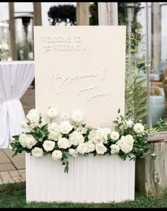 a welcome sign with white flowers and greenery in front of a wedding reception table