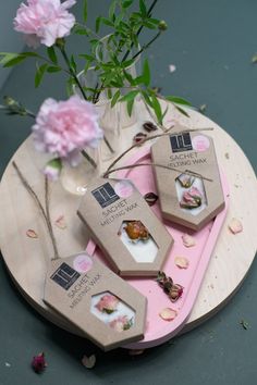 three small boxes with flowers in them on a pink tray next to a flower vase