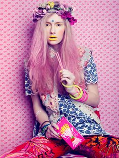 a woman with pink hair sitting on top of a bed holding an object in her hand