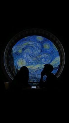 two people sitting in front of a window with the starry night painting on it