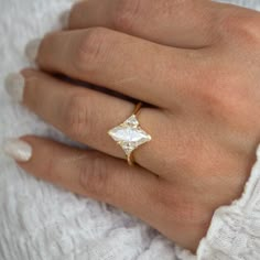 a woman's hand wearing a gold ring with a square shaped diamond on it