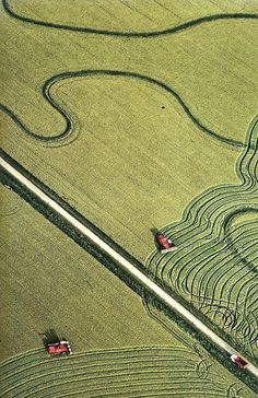 an aerial view of two cars driving down a road in the middle of a field