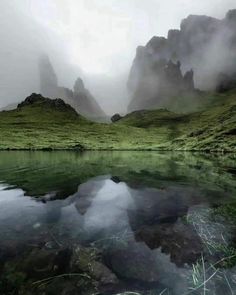 the mountains are covered in fog and mist as they sit on top of a body of water