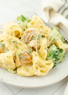 a white plate topped with pasta and broccoli covered in cheese sauce next to a fork